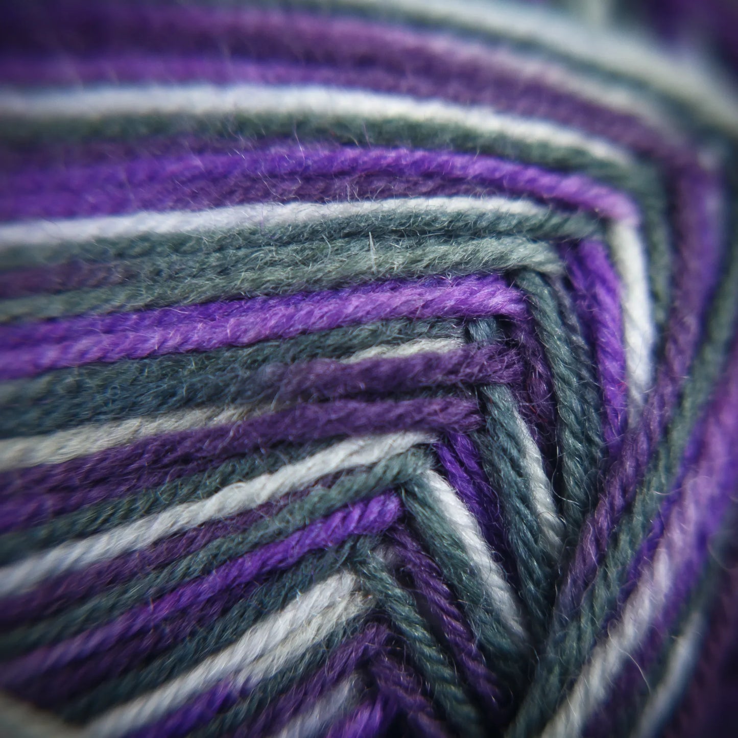 Macro close-up of Purple Ivy yarn fibres featuring dusky lavenders, aubergine and near-black blending.