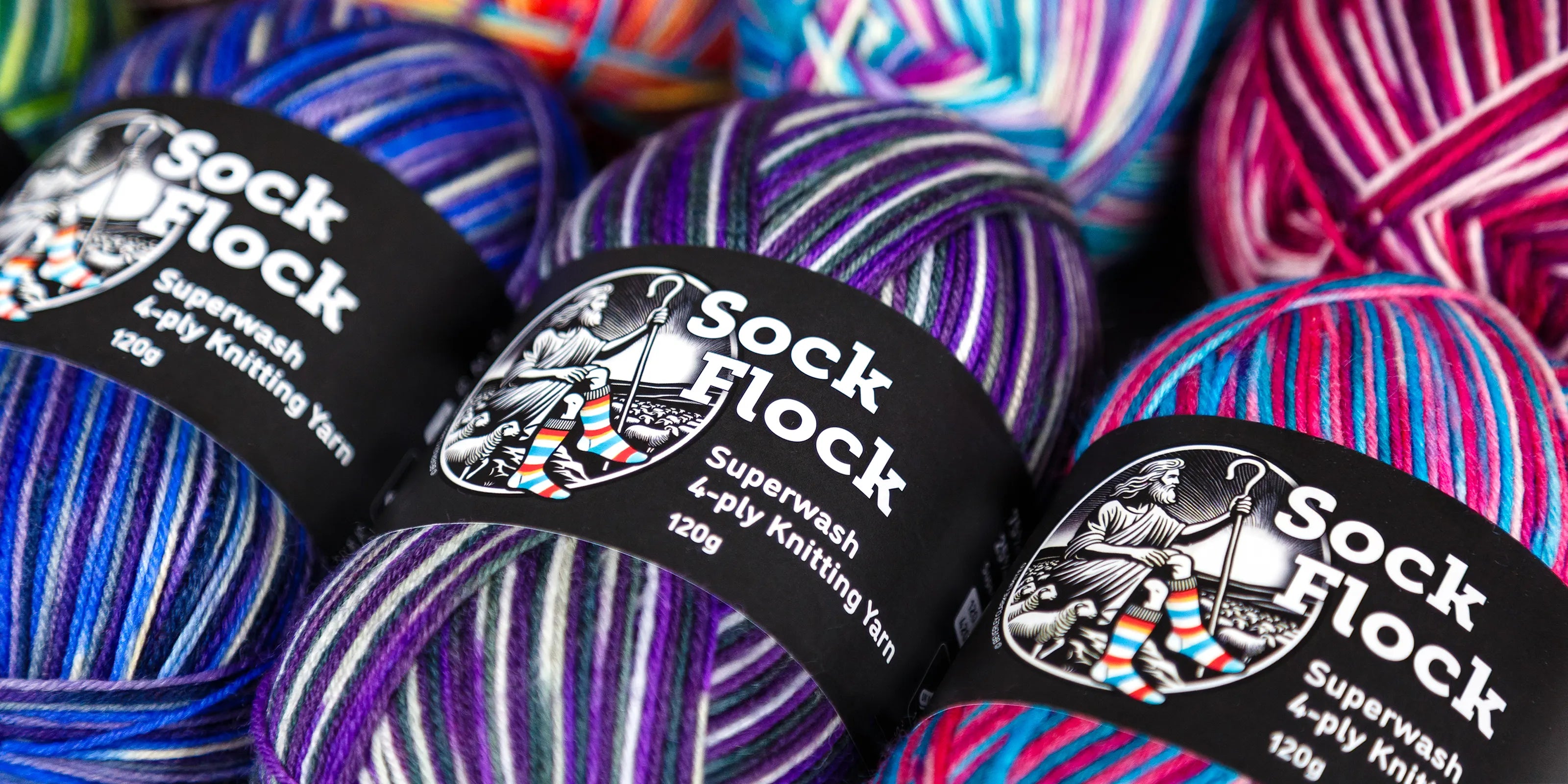 Artistic shallow-focus shot of Purple Ivy yarn ball surrounded by Blue Moon and Sakura Spring, highlighting subtle variegation and tightly spun wool textures.