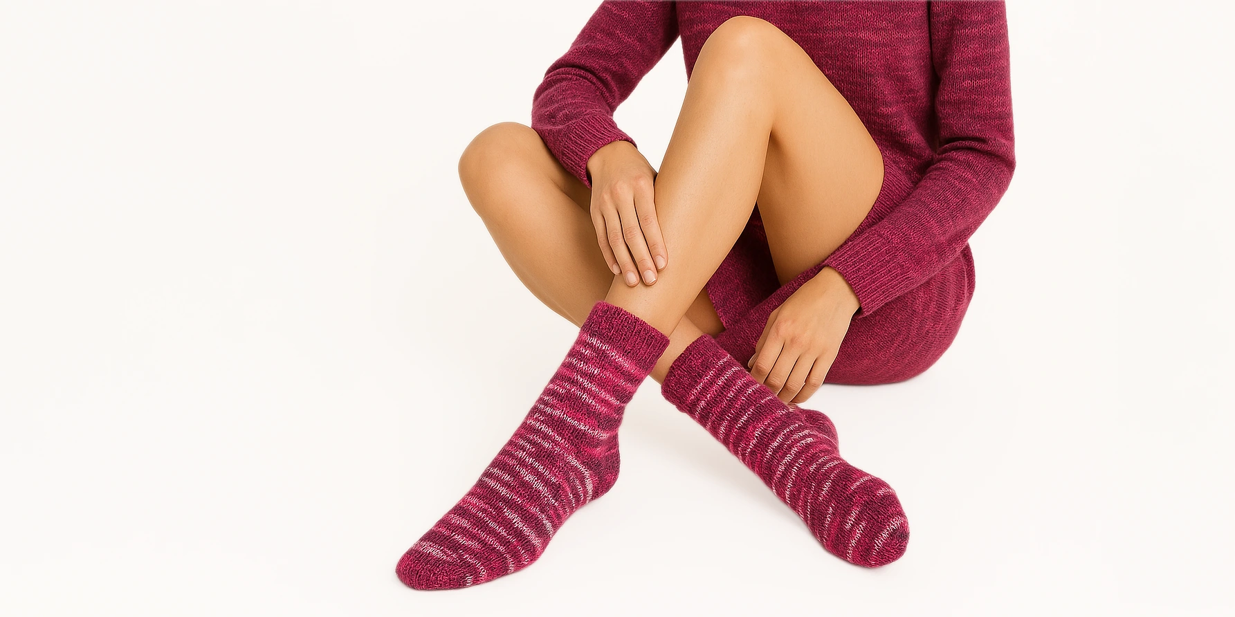 Model wears soft jumper and matching self-striping socks in a Sock Flock colourway, seated on a rustic wooden chair with natural light falling on wool textures.