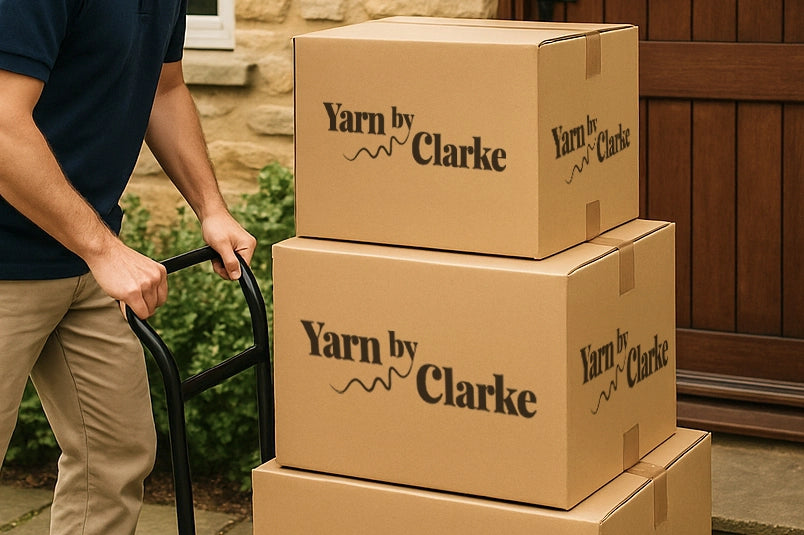 Close-up of cardboard delivery boxes with Yarn by Clarke logo stacked on a hand truck outside a customer’s front door.